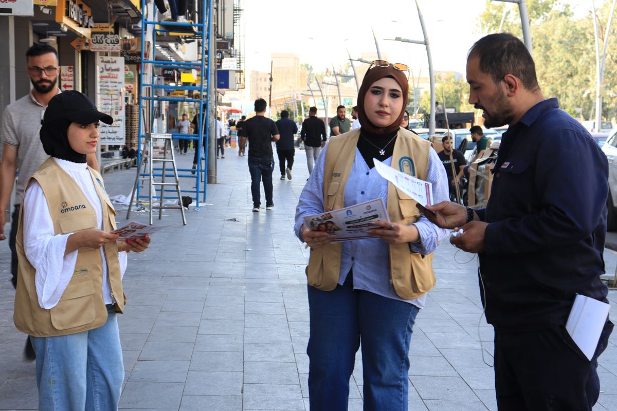 Two AGO volunteers sharing campaign flyers with a man on a busy street