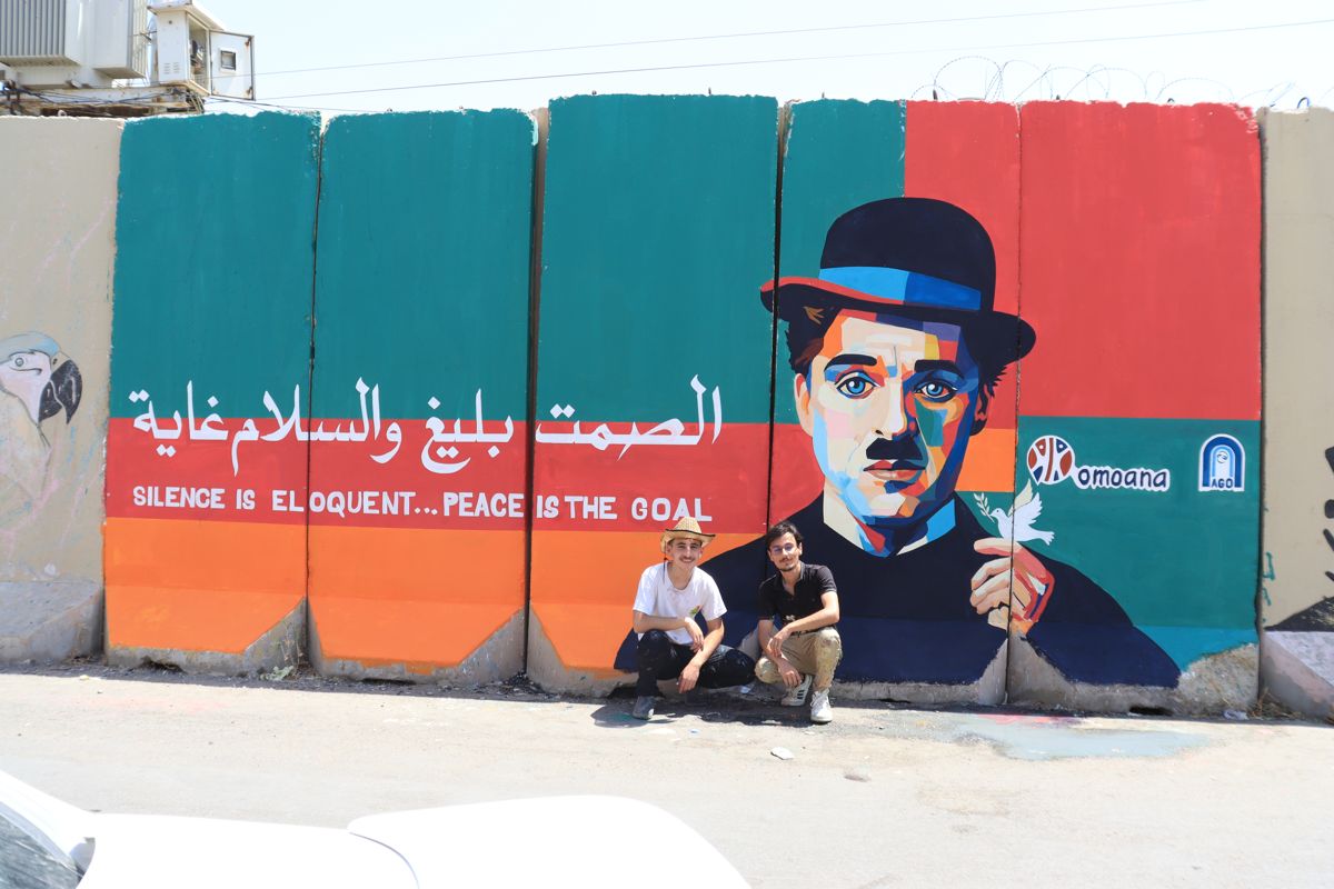 Two young artists in front of the “Silence is eloquent… peace is the goal” mural